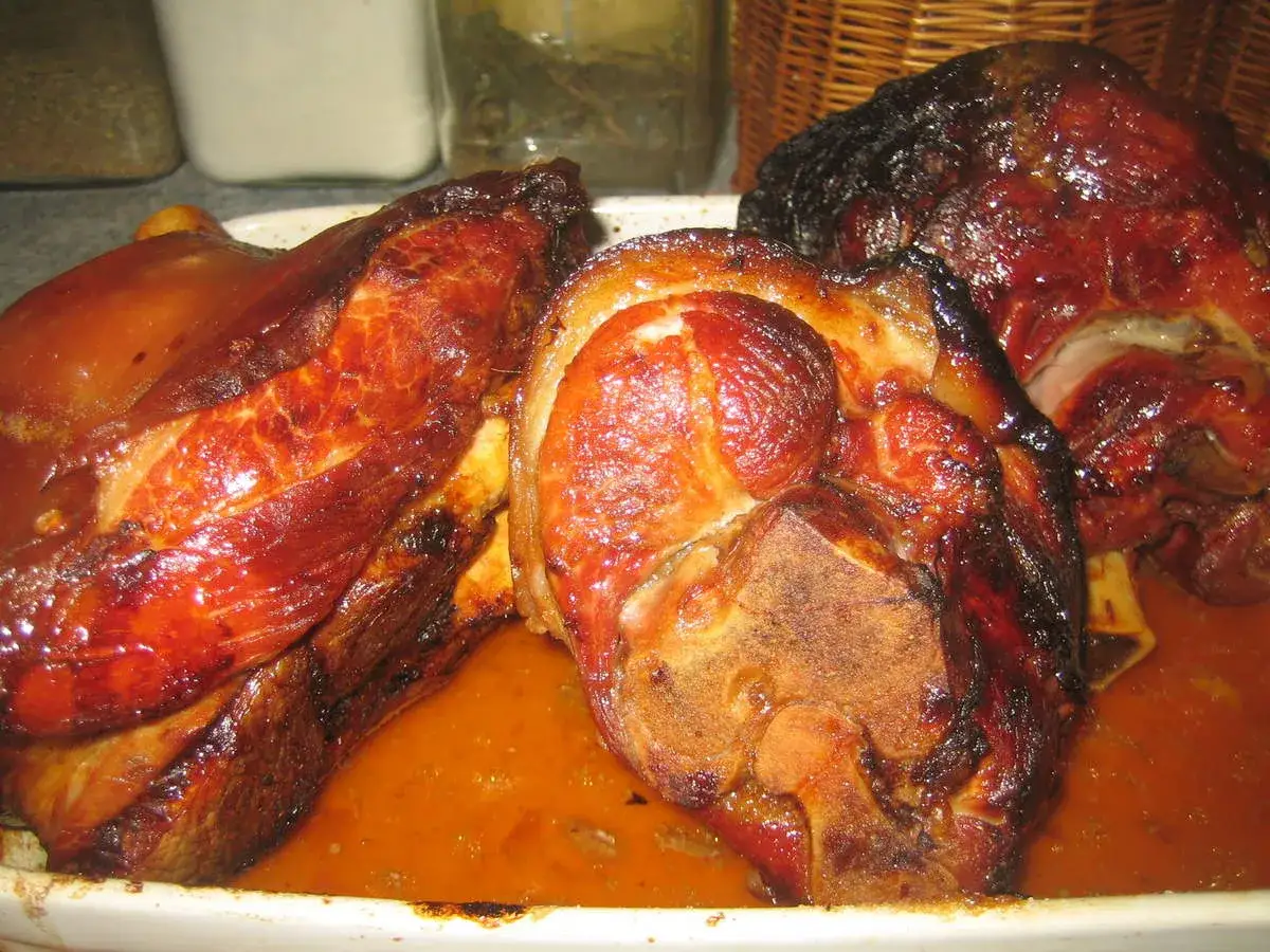 Trois jarrets de porc rôtis, brillants et juteux, baignant dans leur jus savoureux.