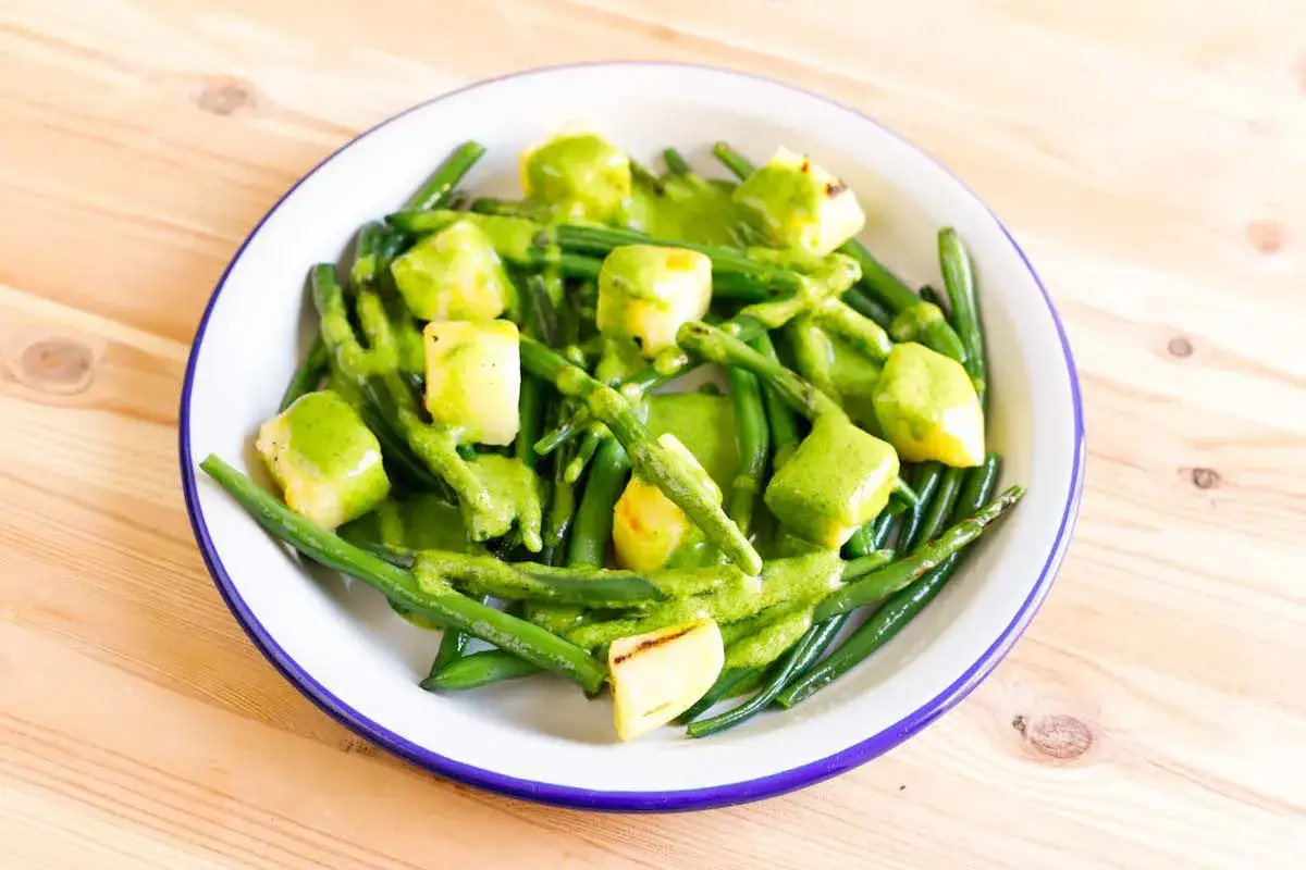 Un piatto di fagiolini e patate conditi con una salsa verde cremosa.