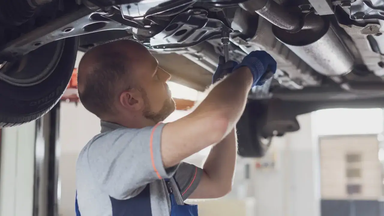 Mechanik w rękawiczkach dokręca śrubę pod samochodem. Szybka wymiana oleju i filtr&oacute;w to klucz do sprawnego działania auta.