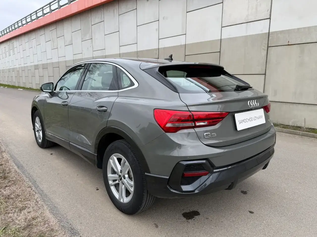 Szary SUV Audi Q3, samochód używany do 70 tys. zł, zaparkowany przy betonowym murze.