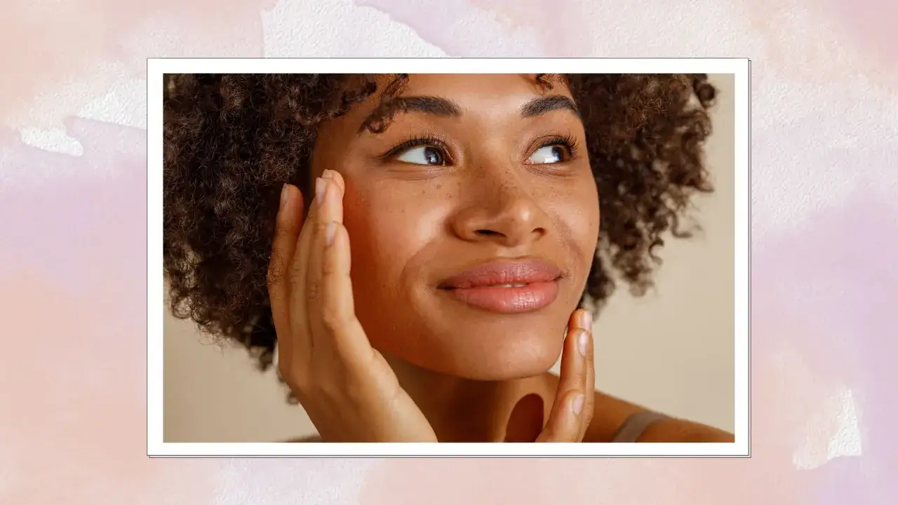 En kvinna med lockigt hår rör vid sitt ansikte, som visar tecken på hormonell acne.