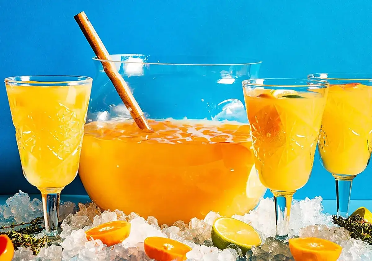 Un refrescante **agua de valencia** servida en copas y ponchera, rodeada de hielo, rodajas de naranja y lima.