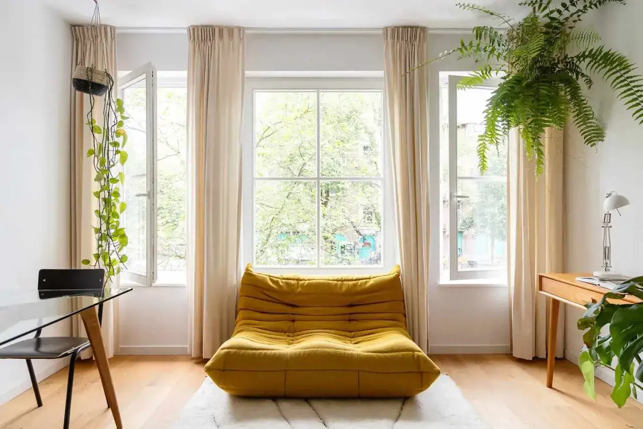 Jasny salon w stylu skandynawskie boho. Ż&oacute;łta kanapa, wiszące rośliny i drewniane meble tworzą przytulną atmosferę.