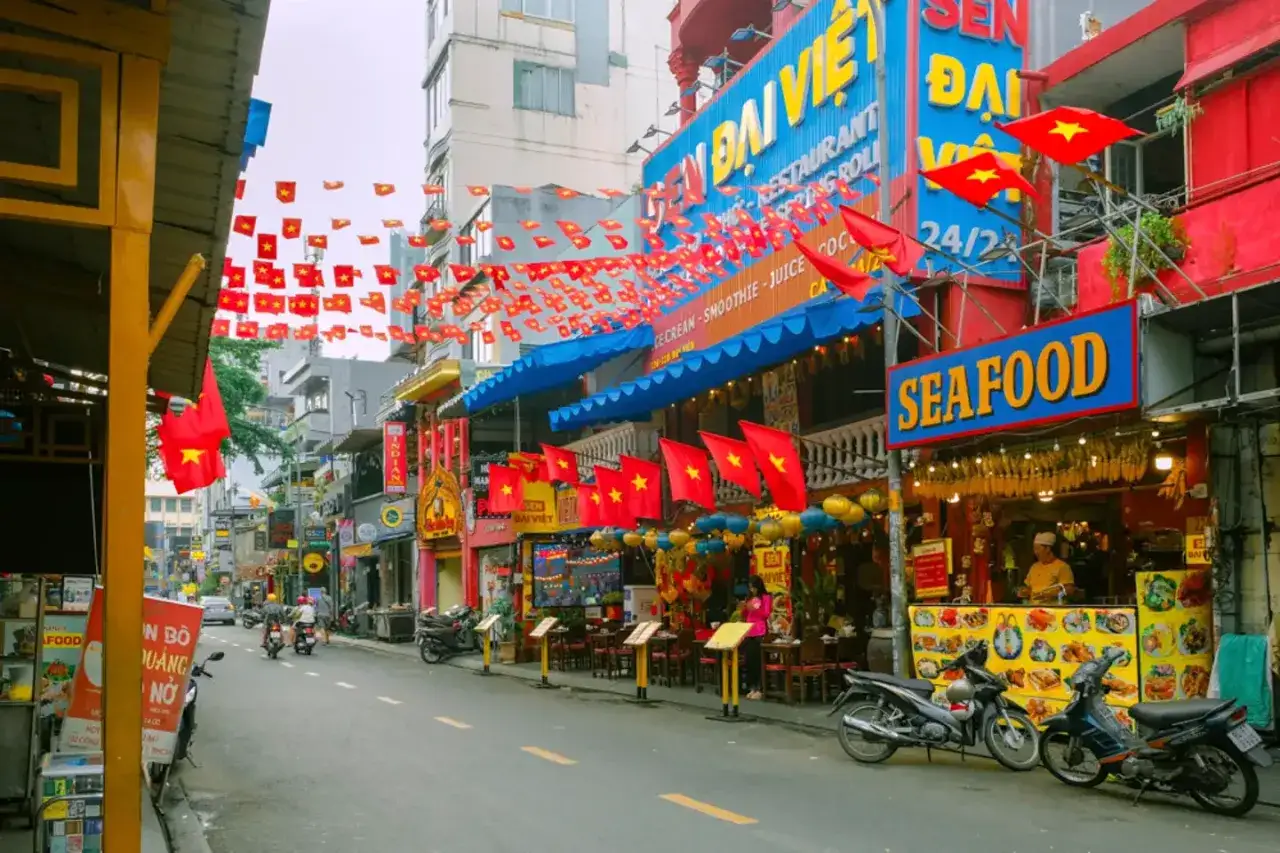 Ulica w Ho Chi Minh Miasto, ozdobiona czerwonymi flagami Wietnamu. Widać restauracje, skutery i gwarne życie miasta.