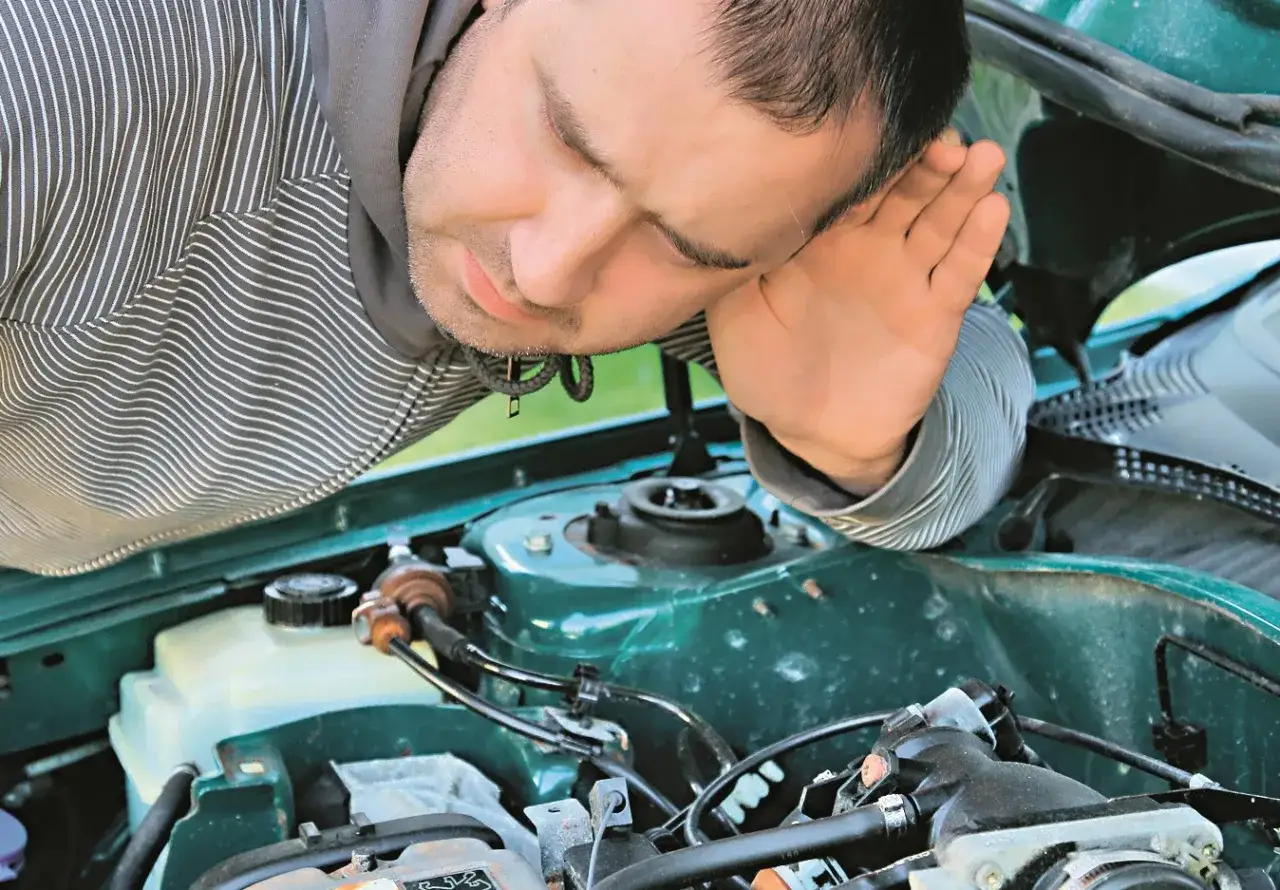 Mężczyzna pochyla się nad silnikiem, próbując zdiagnozować, dlaczego auto nie odpala.