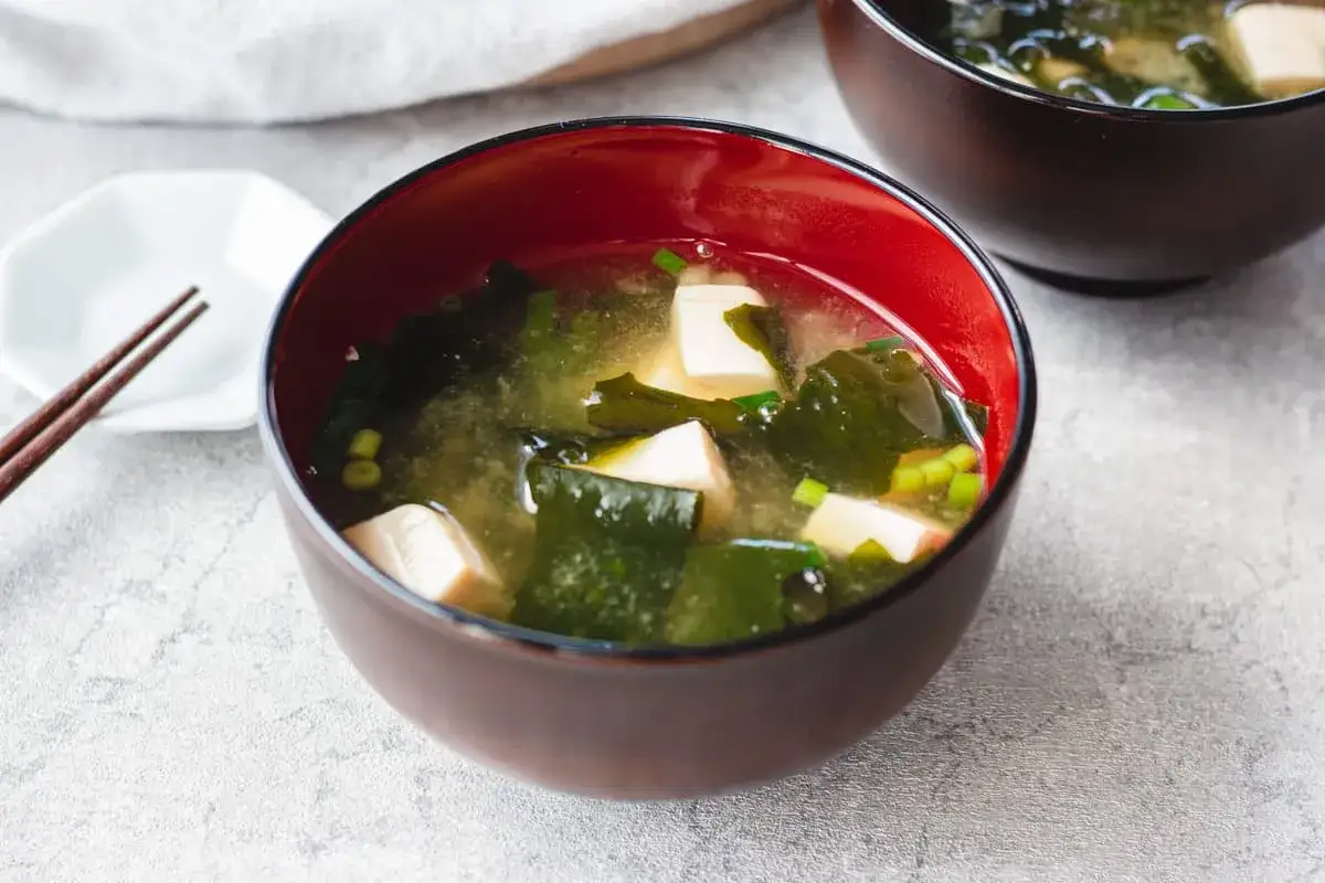 A steaming bowl of nori soup with tofu and green onions, ready to be enjoyed with chopsticks.