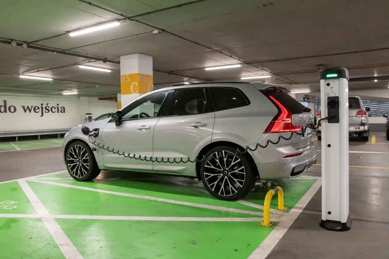 Srebrne Volvo XC60 na zielonym polu ładowania. Dylemat: volvo xc60 jaki silnik wybrać? Elektryczny czy hybrydowy?