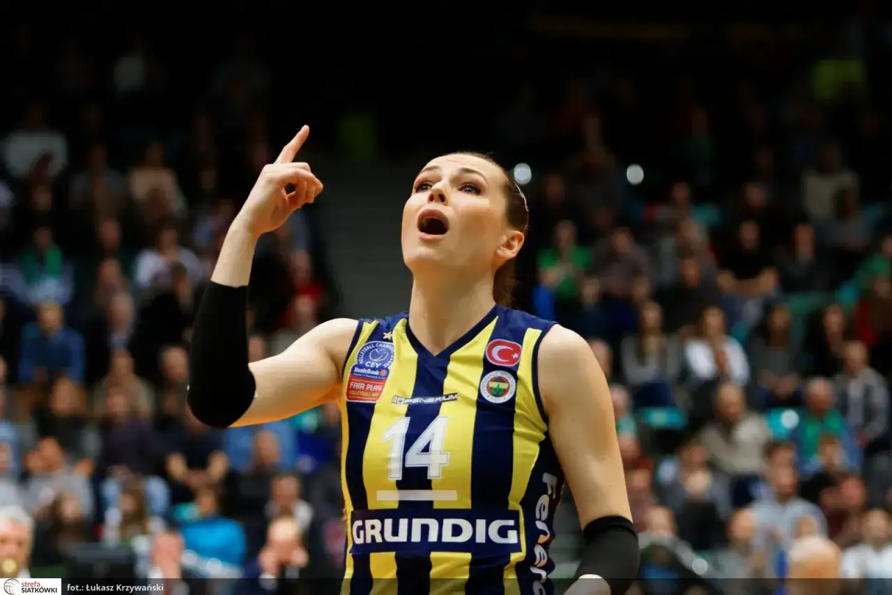 Eda Erdem, z numerem 14 na koszulce, unosi palec wskazujący, krzycząc z radości na boisku siatkarskim.