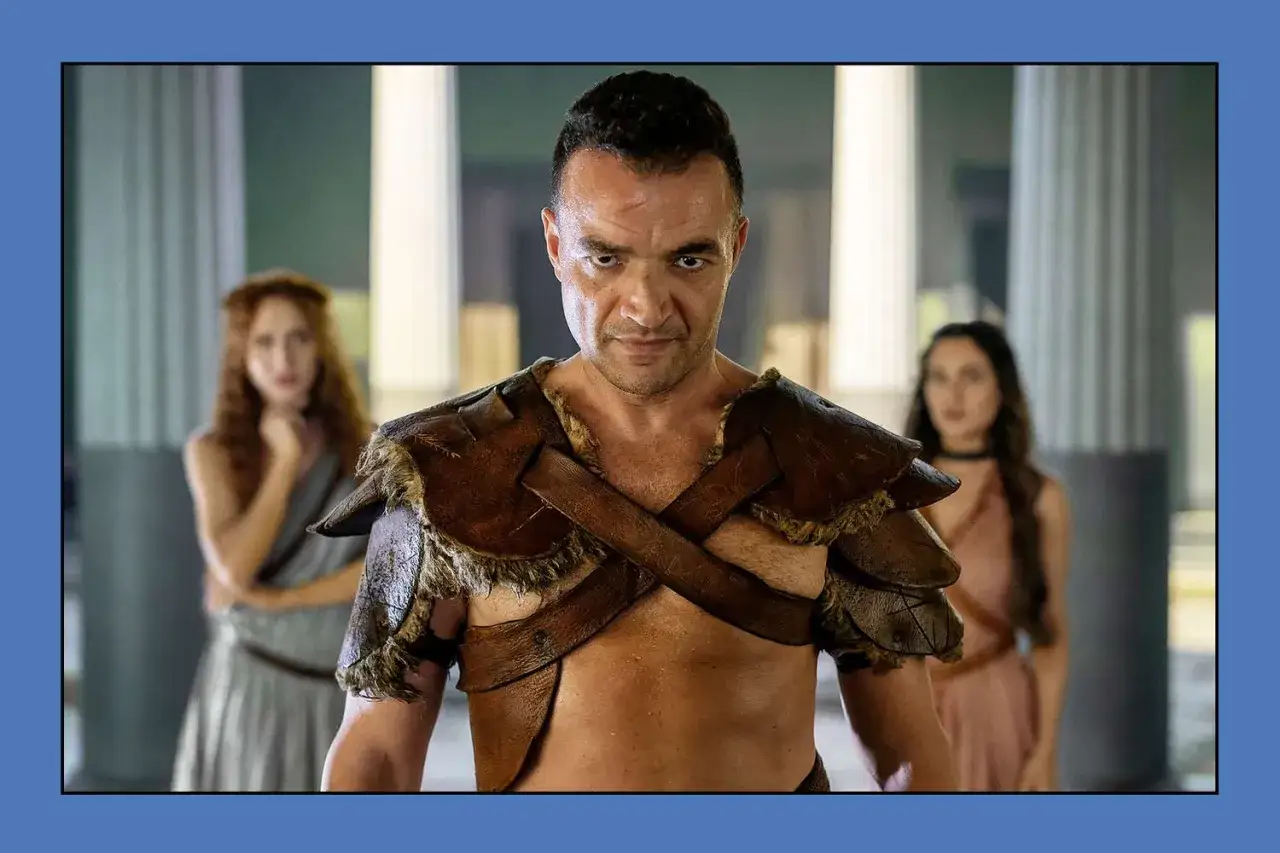 En man i läderrustning, med två kvinnor i bakgrunden, från Spartacus: House of Ashur.