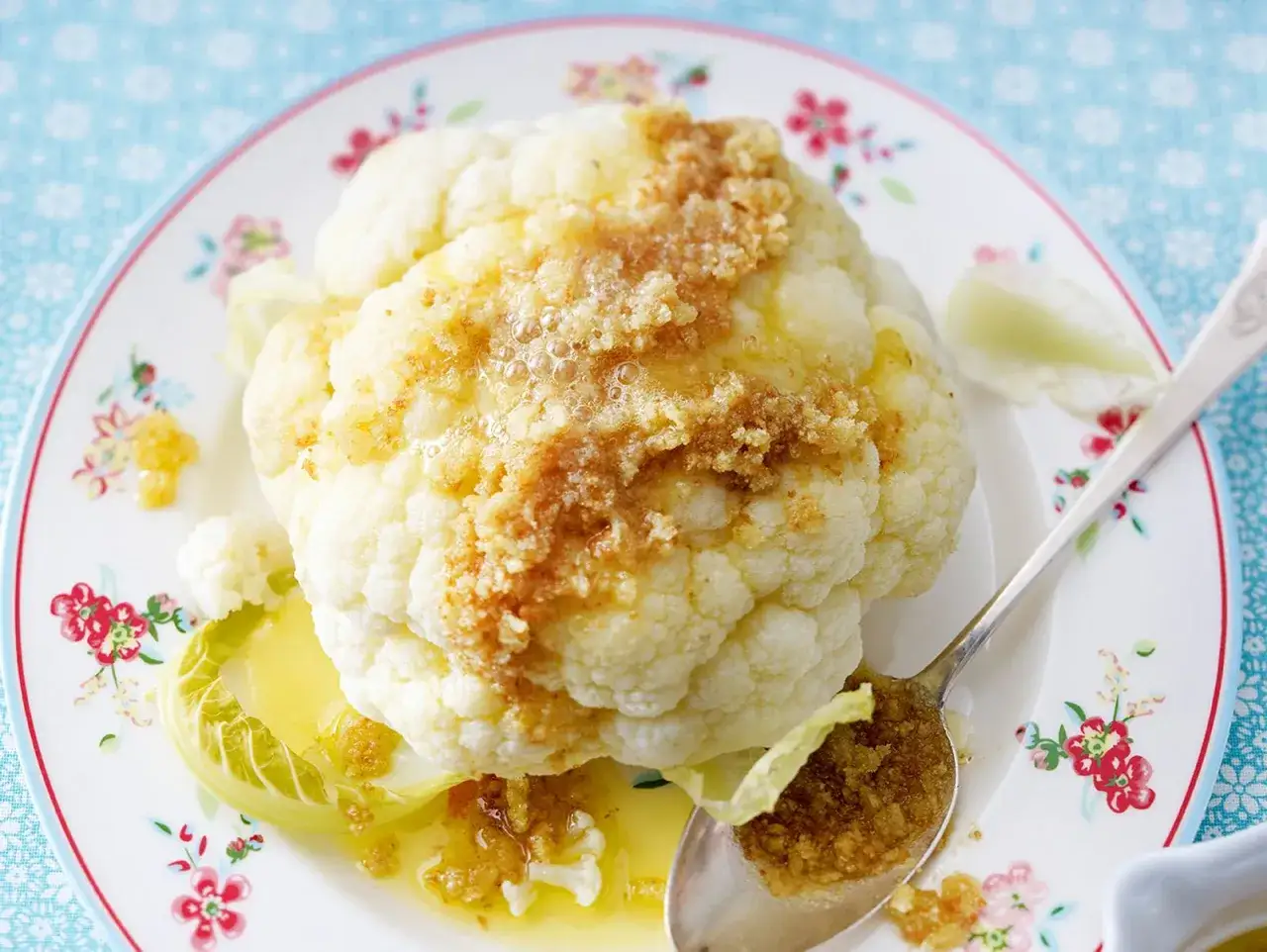 Ganzes Blumenkohl-Rezept mit Butter und Kr&uuml;utern, serviert auf einem Teller mit Blumenmuster.
