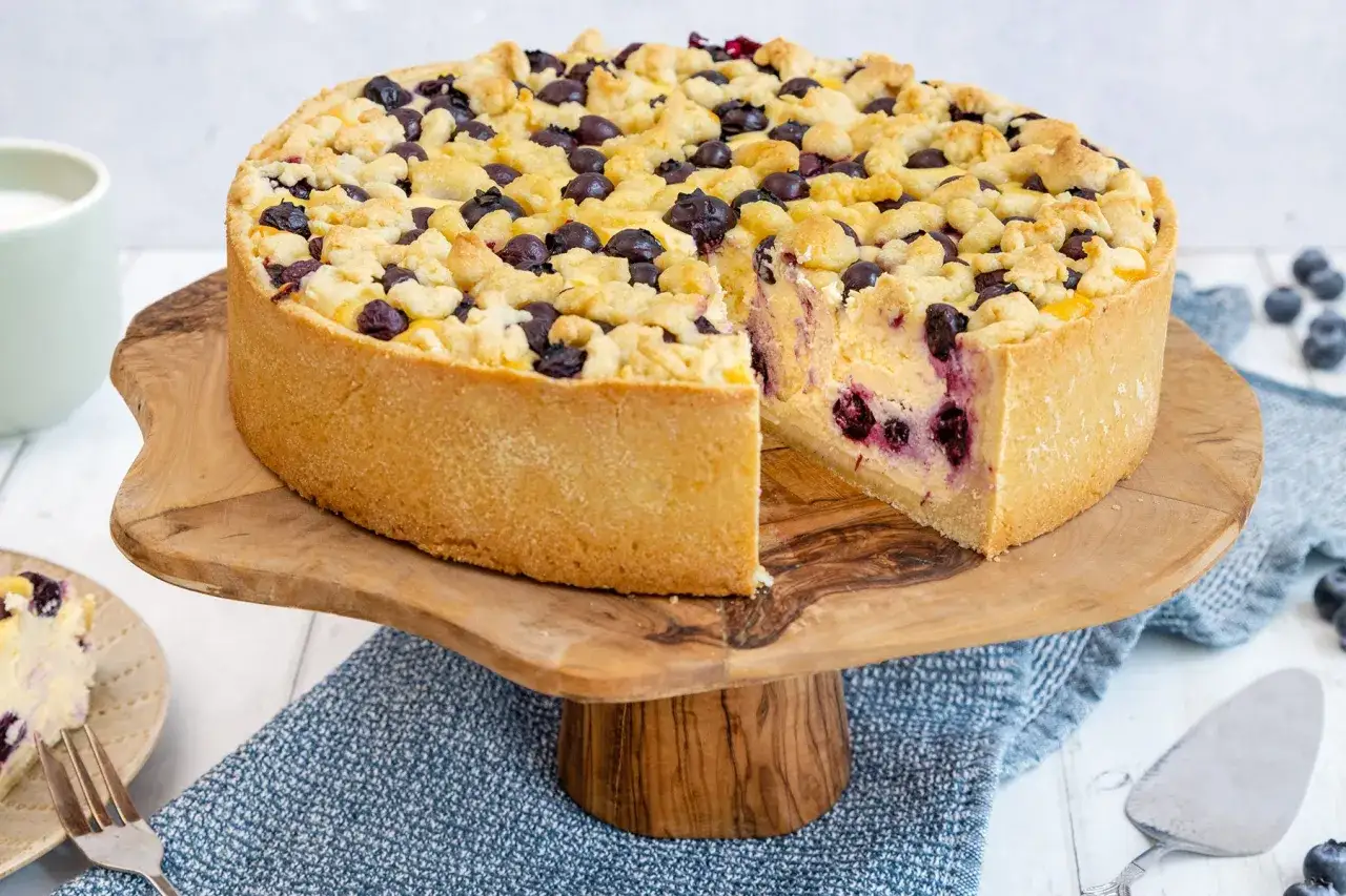 Saftiger Blaubeerkuchen nach Omas Rezept, mit Streuseln und frischen Blaubeeren, auf einem Holzst&auml;nder.