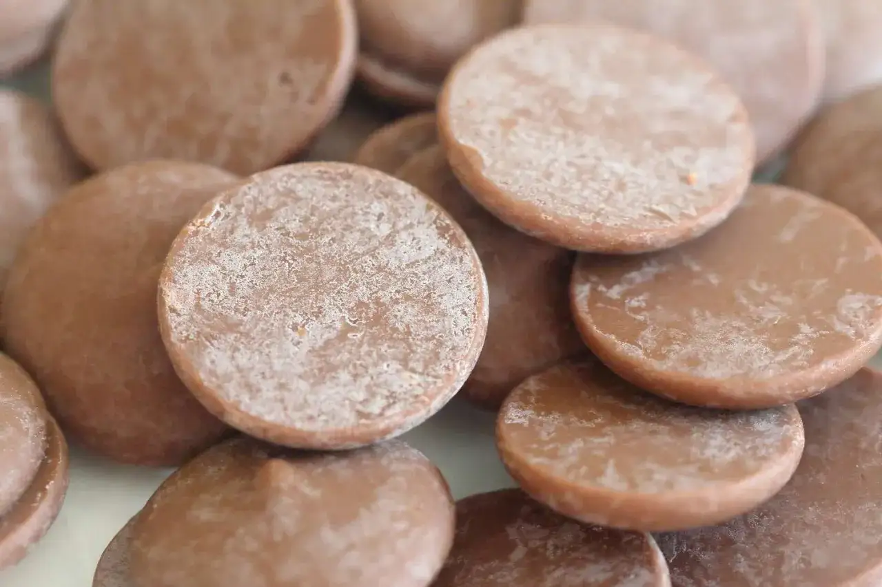 Gros plan sur des pastilles de chocolat au lait, certaines pr&eacute;sentant un l&eacute;ger voile blanc, comme un point blanc chocolat.