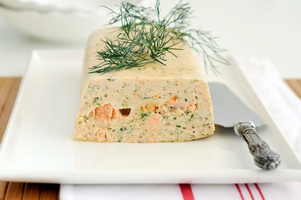 Un pain de poisson savoureux, garni d'aneth frais, est présenté sur une assiette blanche avec un couteau à pâtisserie.