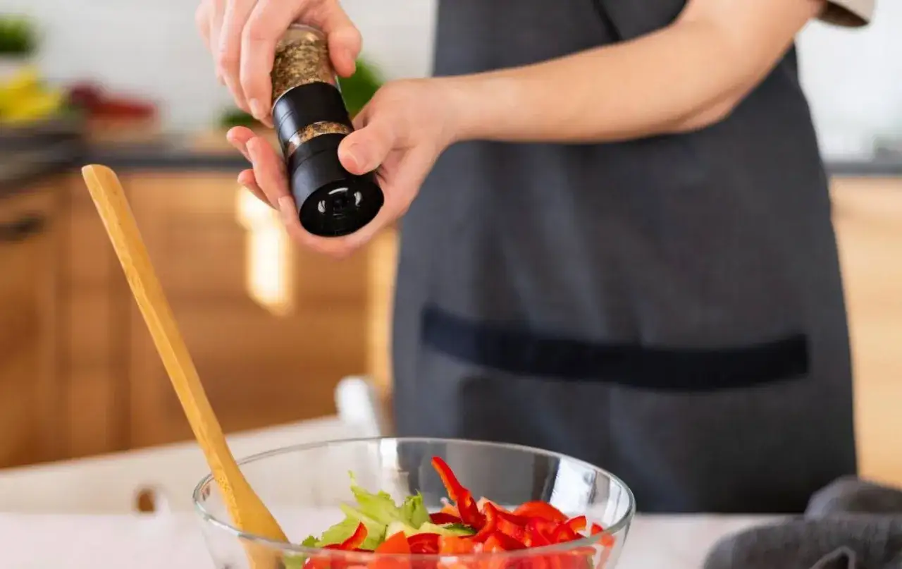 Person w&uuml;rzt Salat mit Pfeffer. So kann man den Zimt Geschmack neutralisieren, wenn er zu dominant ist.