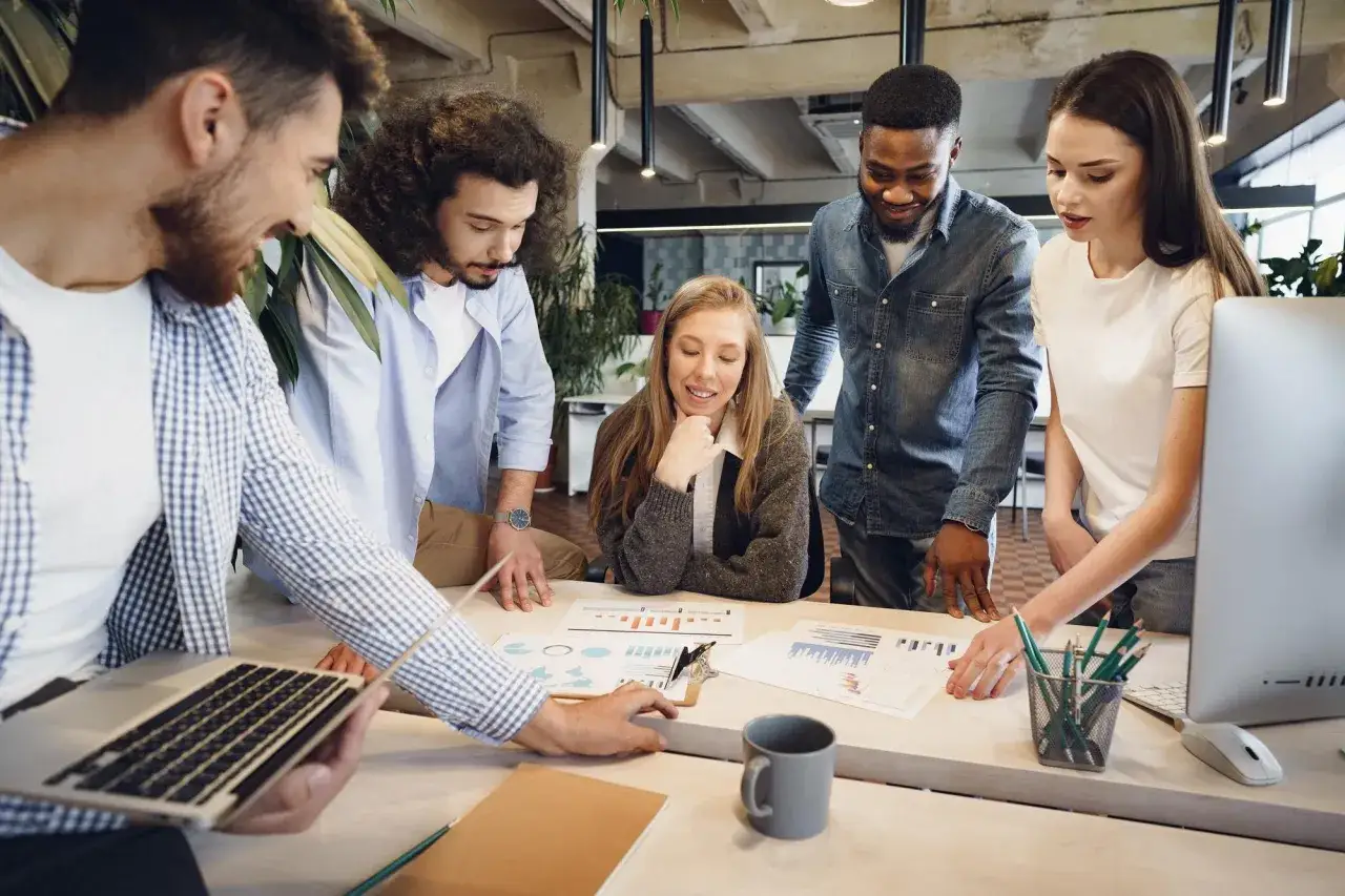 A diverse team collaborates around a table, discussing charts and graphs. This is what employee engagement looks like: focused, collaborative, and productive.