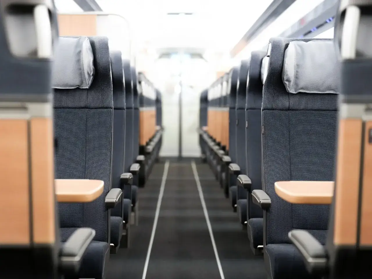 Reihe von Sitzen in einem Zug. Die Sitze sind dunkelblau mit hellgrauen Kopfst&uuml;tzen und Holzakzenten. Der Gang ist mit einem schwarzen Teppich ausgelegt. Der Zug ist bereit f&uuml;r den **ice service**.
