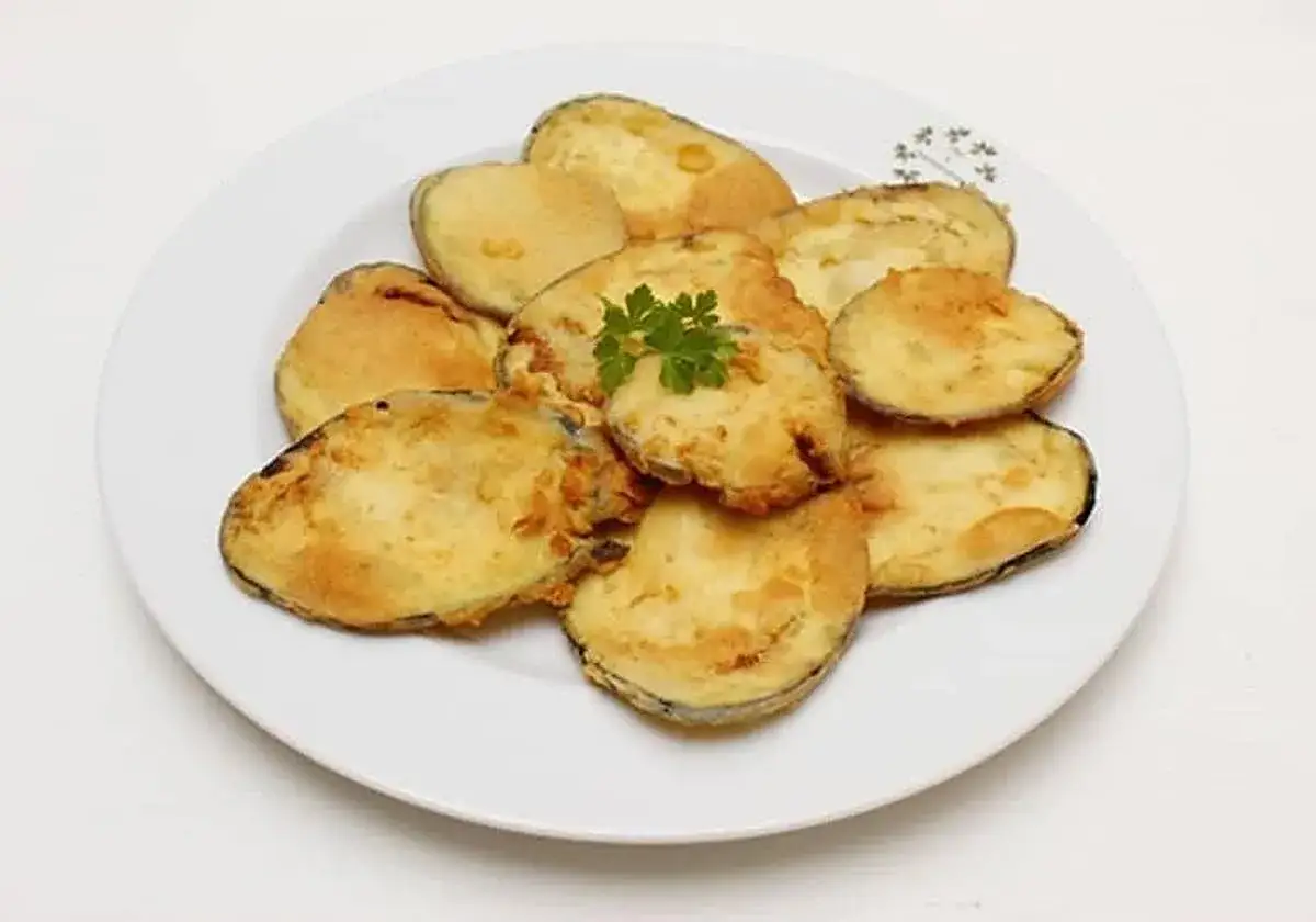 Berenjenas fritas doradas y crujientes, perfectas para aprender cómo hacer berenjenas fritas. Decoradas con perejil fresco.