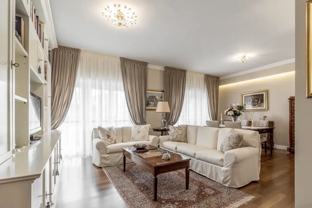 Soggiorno elegante con divani bianchi, tappeto persiano e tende color tortora che si abbinano perfettamente al divano, creando un'atmosfera accogliente.