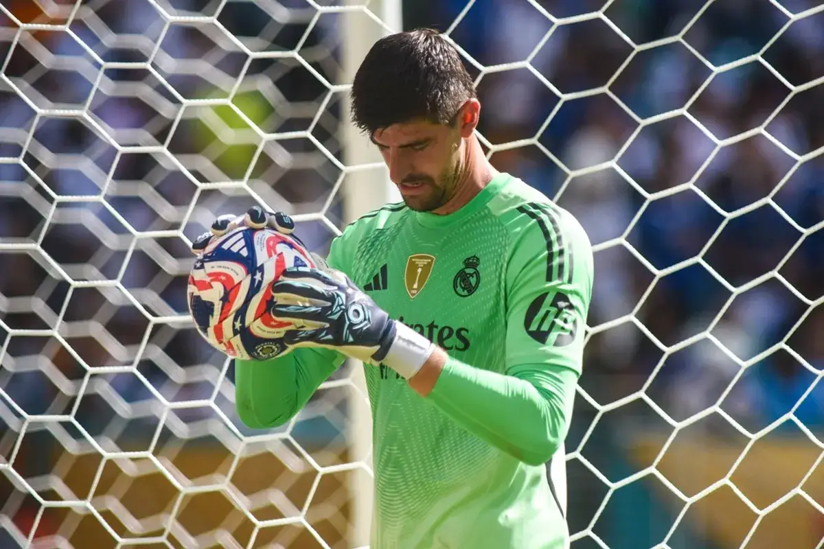 Bramkarz Realu Madryt, Thibaut Courtois, trzyma piłkę w rękawicach, gotowy do obrony bramki.