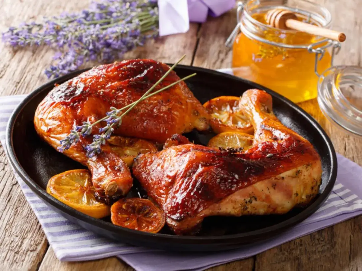 Muslos de pollo al horno dorados y jugosos, servidos con rodajas de limón y un toque de lavanda. Un tarro de miel dorada acompaña este delicioso plato.