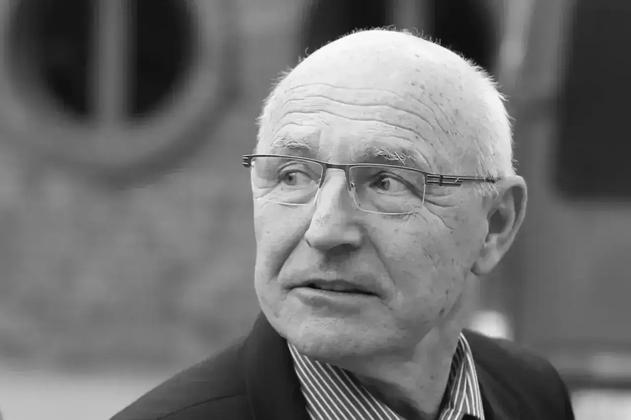 Portret starszego mężczyzny w okularach, z siwymi włosami. To lenczyk trener piłkarski, zamyślony.