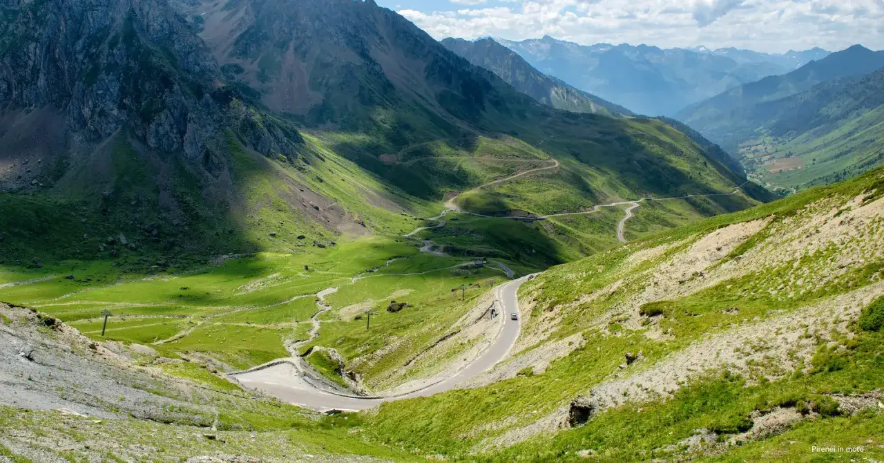 Strada tortuosa sul Col du Tourmalet, con montagne verdi e cielo azzurro. Un'auto percorre il passo.