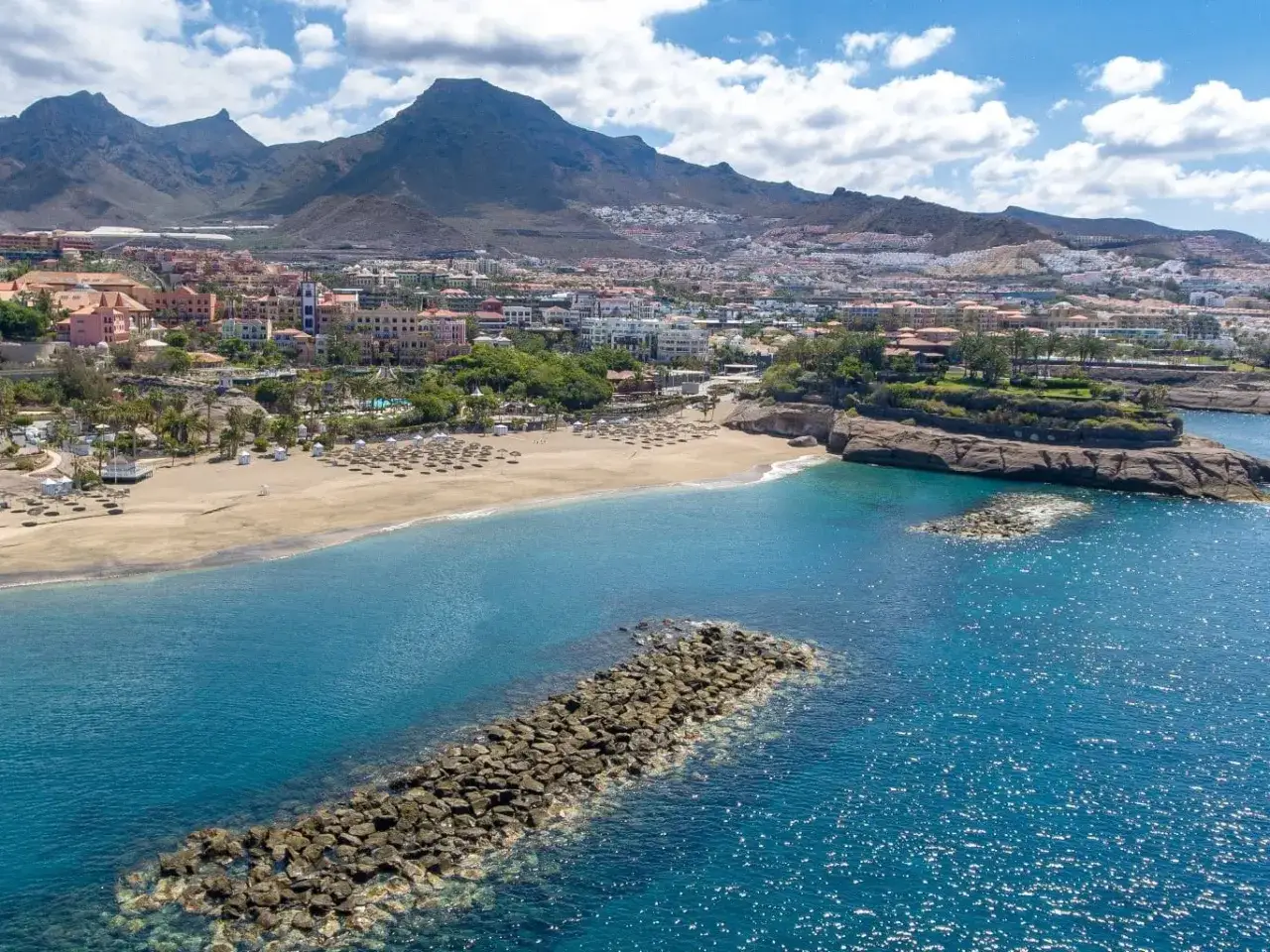 Słoneczne Costa Adeje plaże z turkusową wodą, górami w tle i hotelami. Idealne miejsce na wakacje.