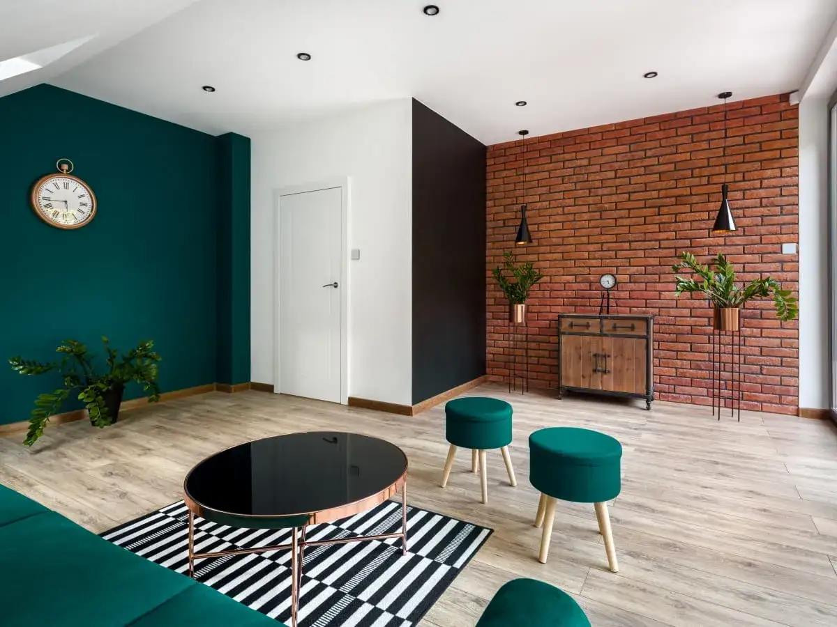 Nowoczesny salon z butelkową zielenią na ścianie, ceglaną ścianą i drewnianą podłogą.