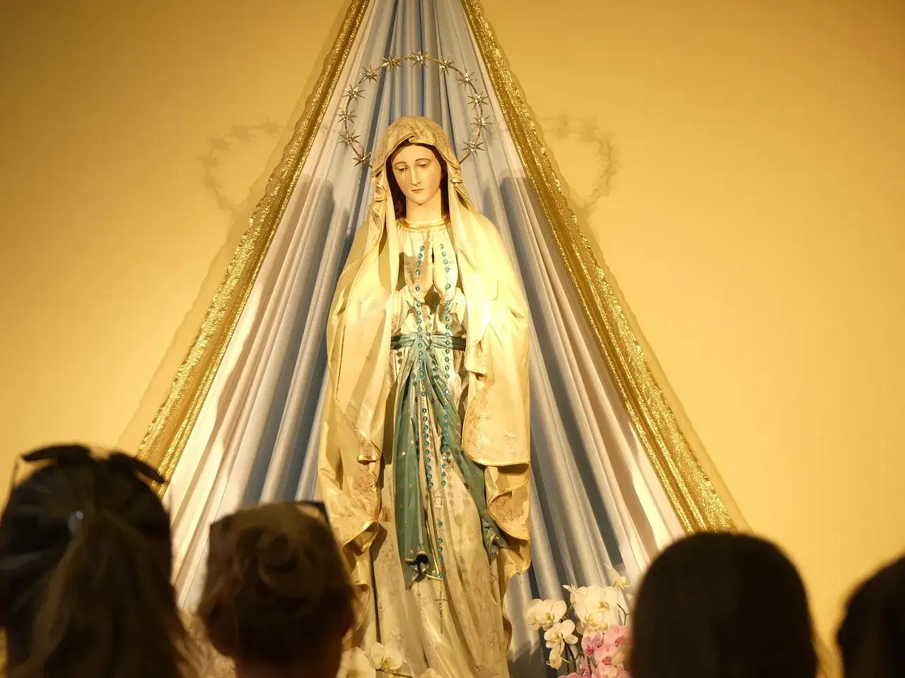 Figurka Matki Boskiej, symbol tradycji, a za nią ludzie, których wiara żywa jest w sercu.