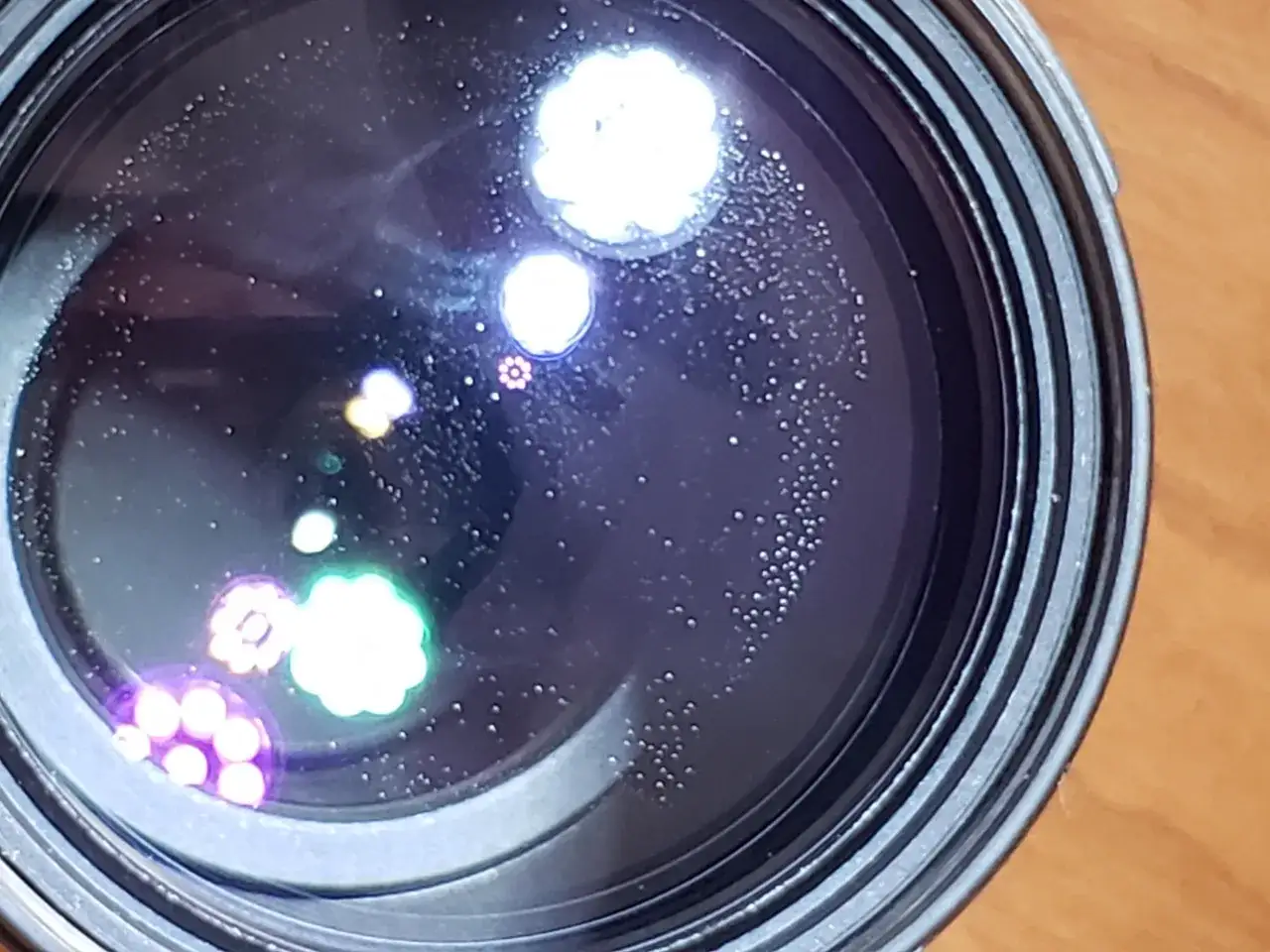 Widoczne na soczewce drobne kropki i poświaty, przypominające aberrację chromatyczną, tworzą na ciemnym tle efekt gwiezdnego nieba.
