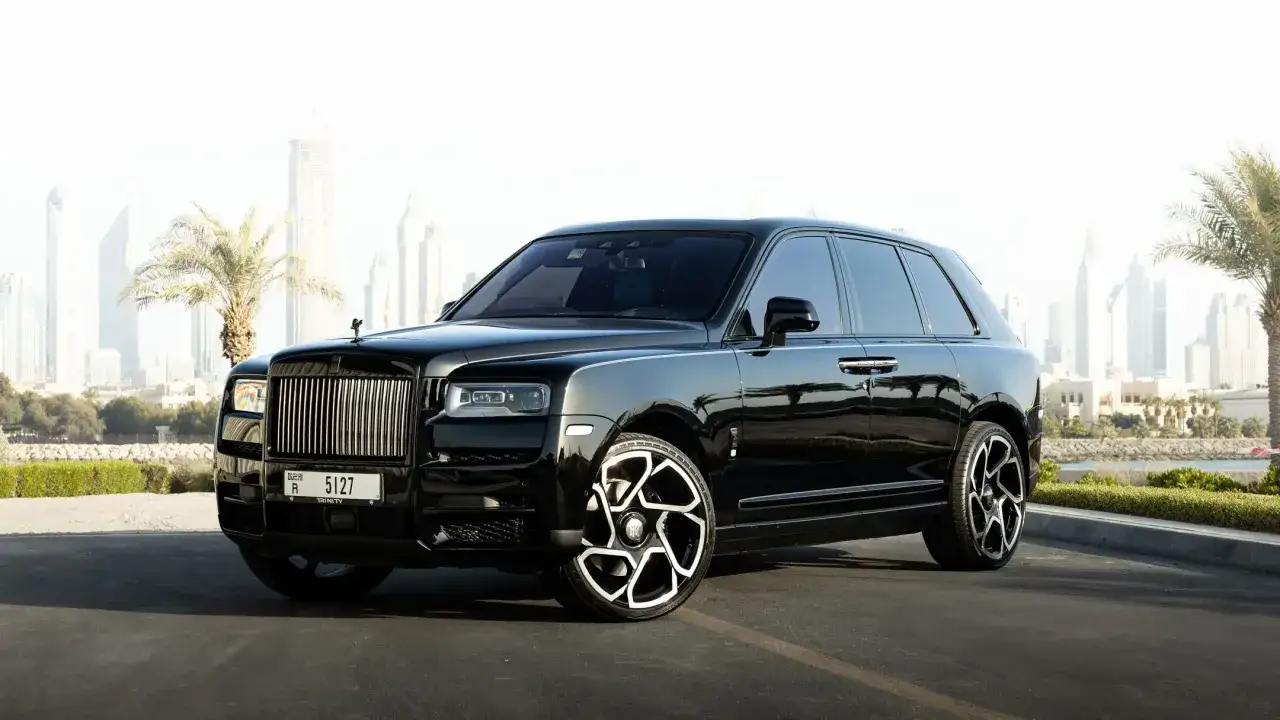 Un Rolls-Royce negro reluciente, perfecto para viajar a Dubái, con palmeras y rascacielos de fondo.