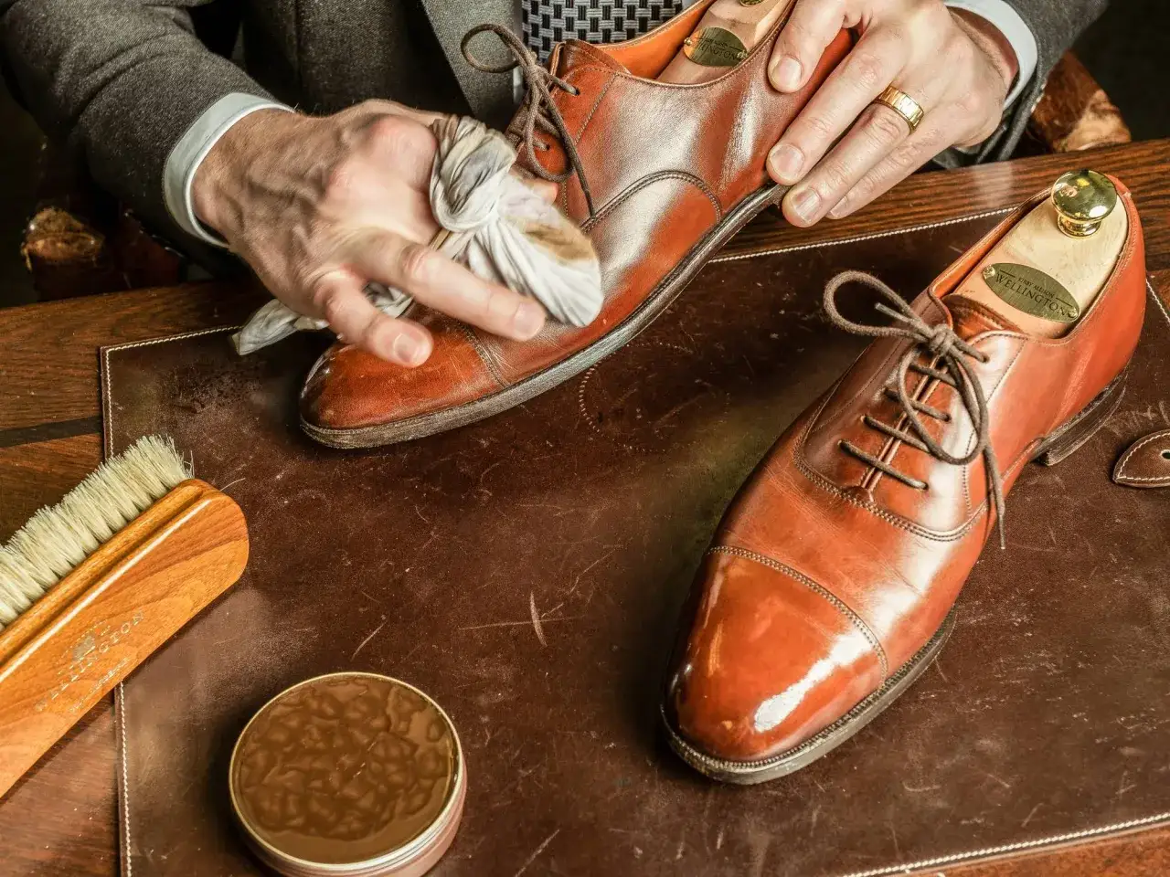 Un homme nettoie ses chaussures en cuir marron clair avec un chiffon. Brosse et cirage &agrave; proximit&eacute; pour un entretien parfait.