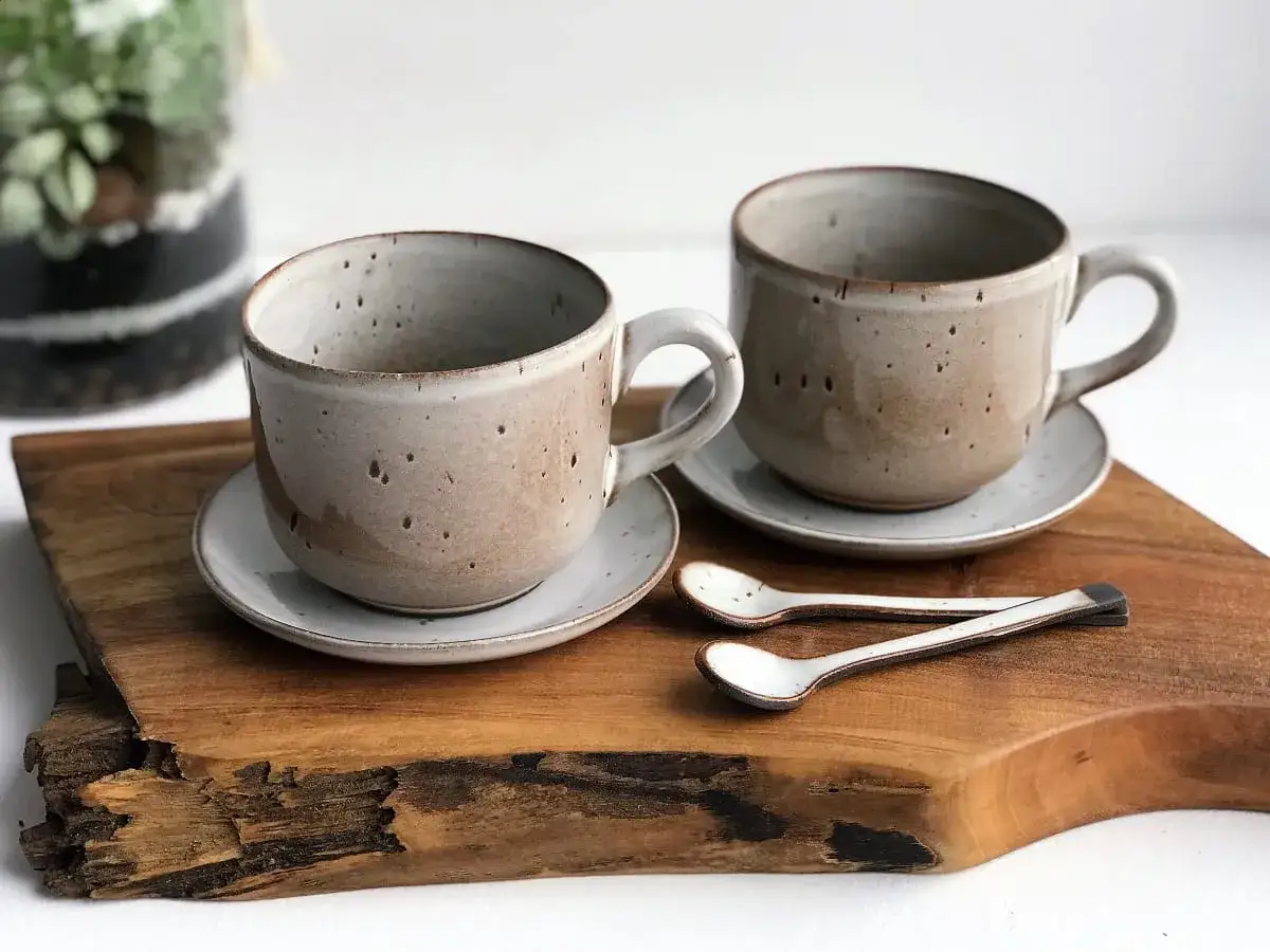 Dwa ceramiczne kubki na spodeczkach, idealne na cappuccino. Ile ml zmieści się w takim kubku? Dwie małe łyżeczki leżą obok.