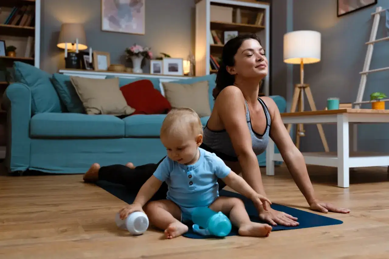 Une mère fait du yoga, un bébé à ses côtés. Elle se concentre sur son exercice périnée post-partum, retrouvant sa force.