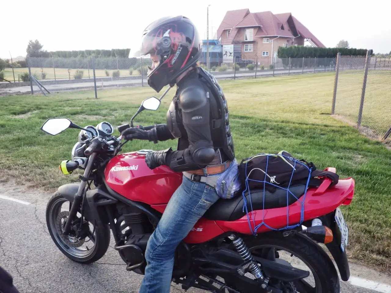 Motocyklista w kasku i ochraniaczach siedzi na czerwonym Kawasaki ER5, gotowy do podróży.