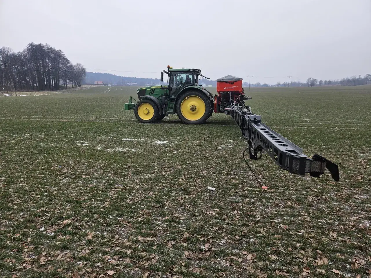 Zielony traktor z opryskiwaczem na polu, przygotowuje się do pracy na wiosnę. Wiosenne zboża już rosną.