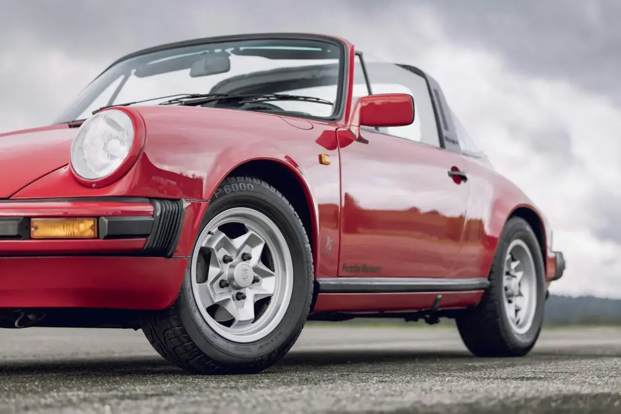 Roter Porsche 911 Targa, ein ikonisches g modell, gl&auml;nzt auf asphaltierter Stra&szlig;e. Das Porsche Museum Logo ist dezent angebracht.