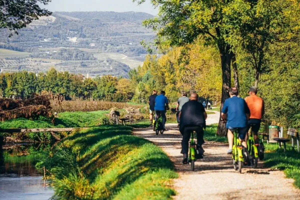 A group enjoys a scenic Verona bike tour along a canal, with rolling hills and autumn foliage in the background.