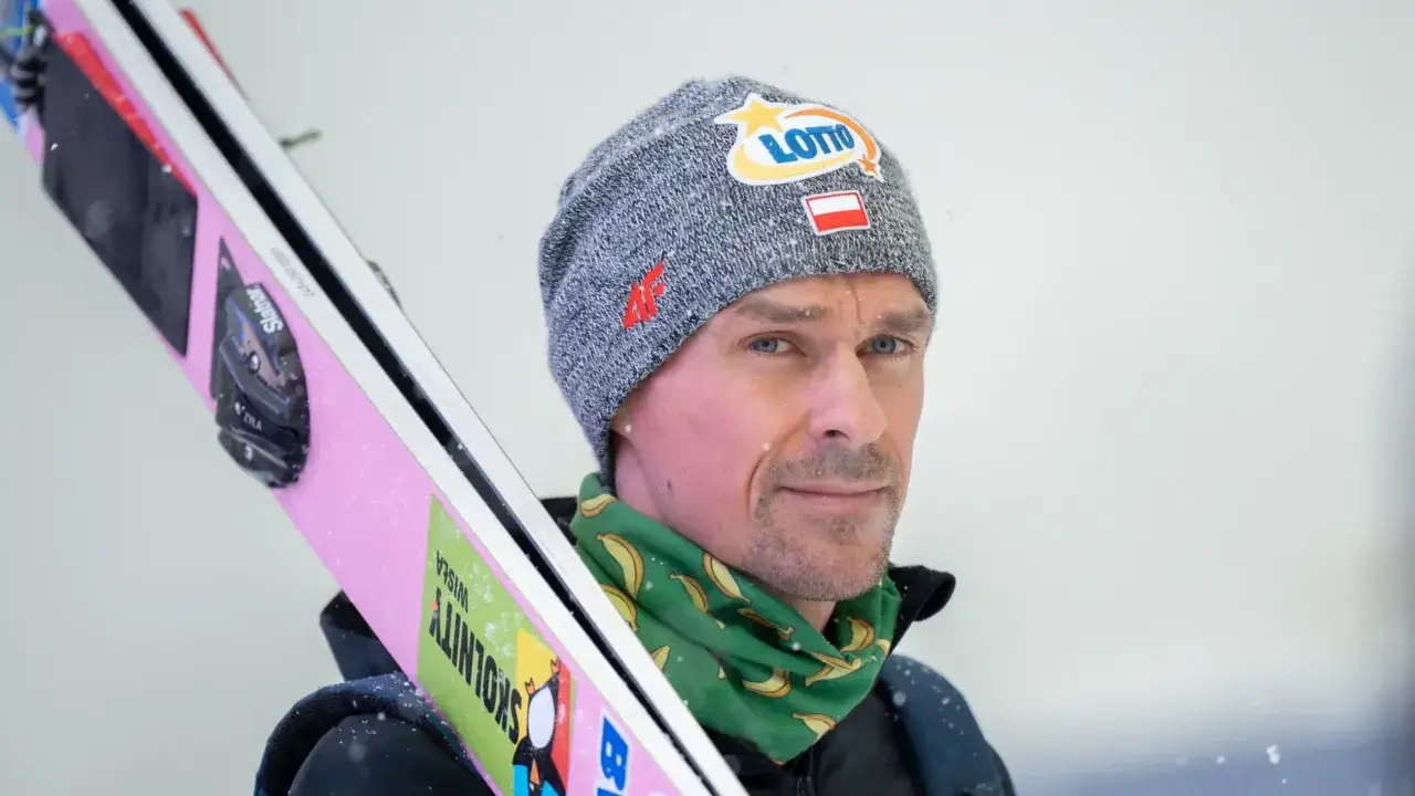 Piotr Żyła, skoczek narciarski, z nartami na ramieniu. Jego czapka z logo Lotto i flagą Polski symbolizuje jego liczne piotr żyła osiągnięcia.