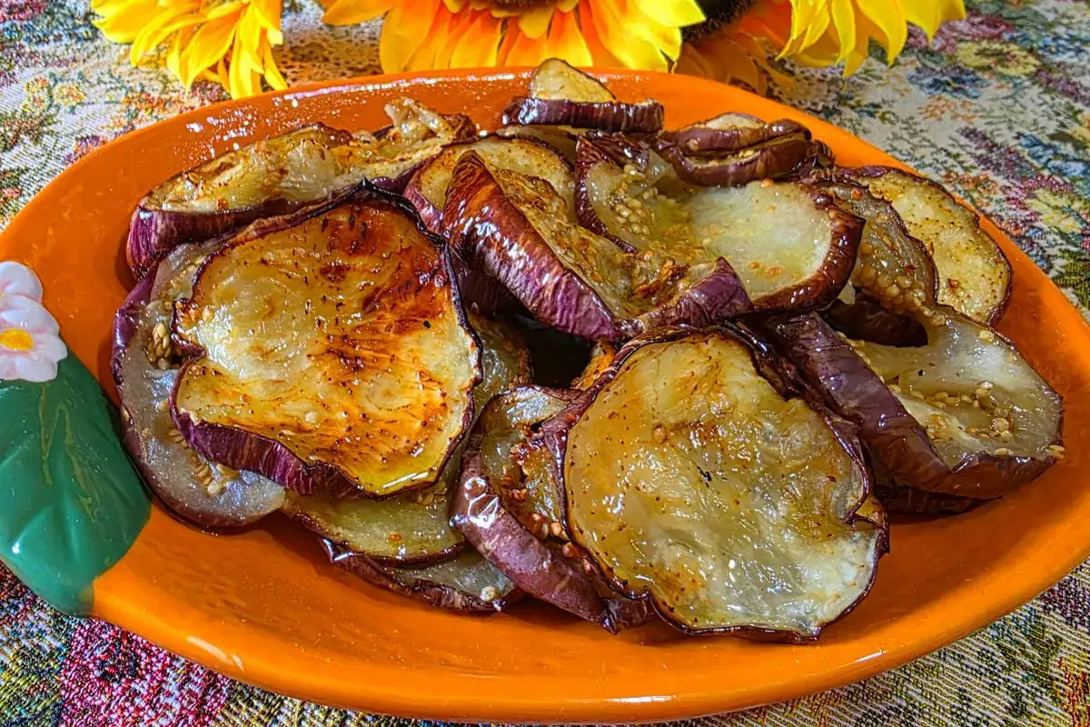 Fette di melanzane dorate e succulente, cotte alla perfezione nella friggitrice ad aria, servite su un piatto arancione decorato.
