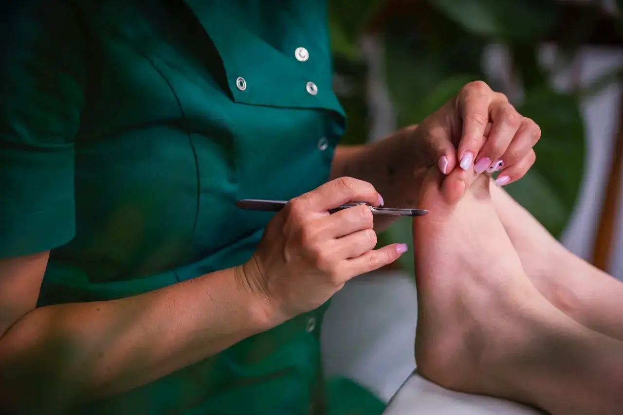 Profesjonalny pedicure to dbanie o stopy. Stylistka w zielonym fartuchu wykonuje zabieg na paznokciach u stóp.