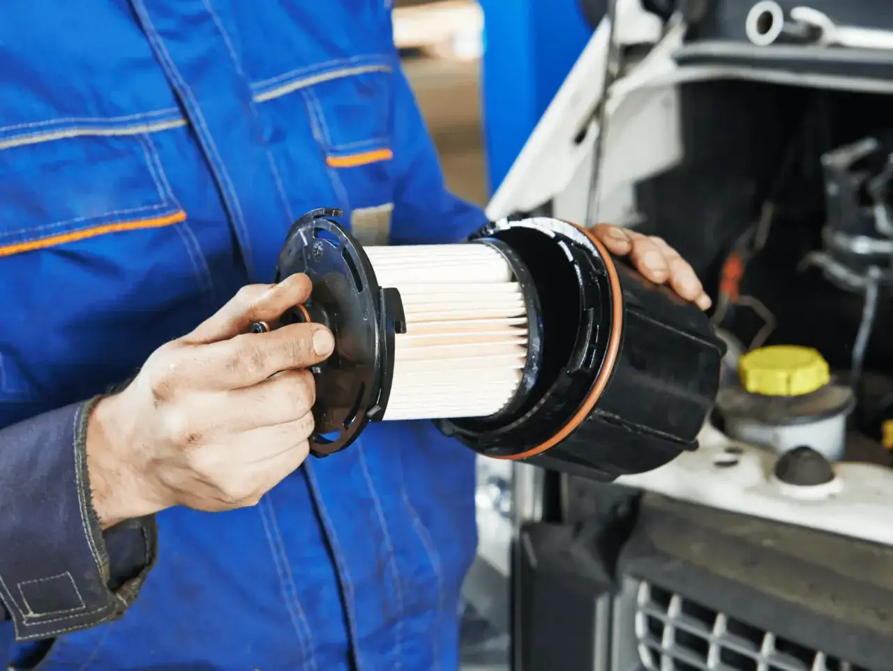 Mecánico con mono azul muestra un filtro de combustible nuevo, listo para instalar y mantener el motor limpio.
