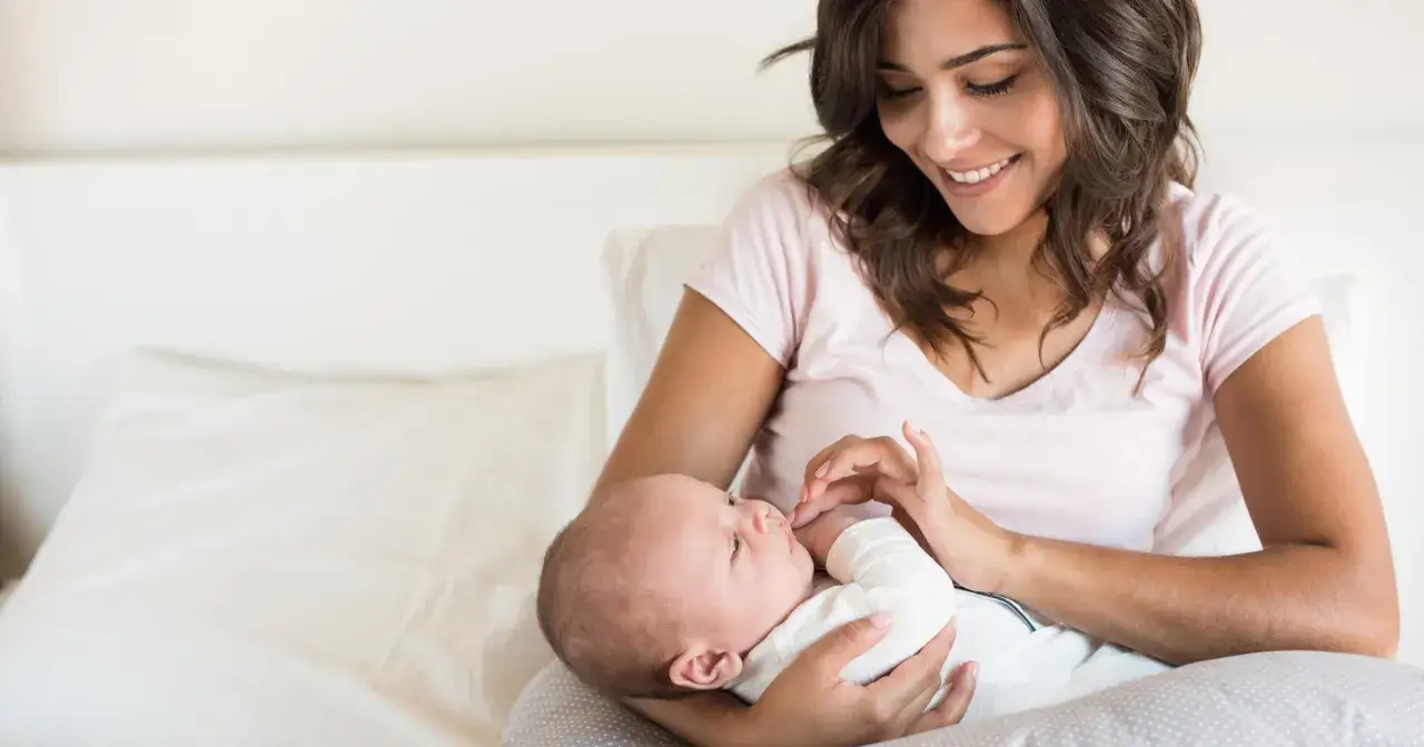 Uśmiechnięta mama tuli noworodka. Czas na odpoczynek po porodzie, zanim pojawią się formalności.