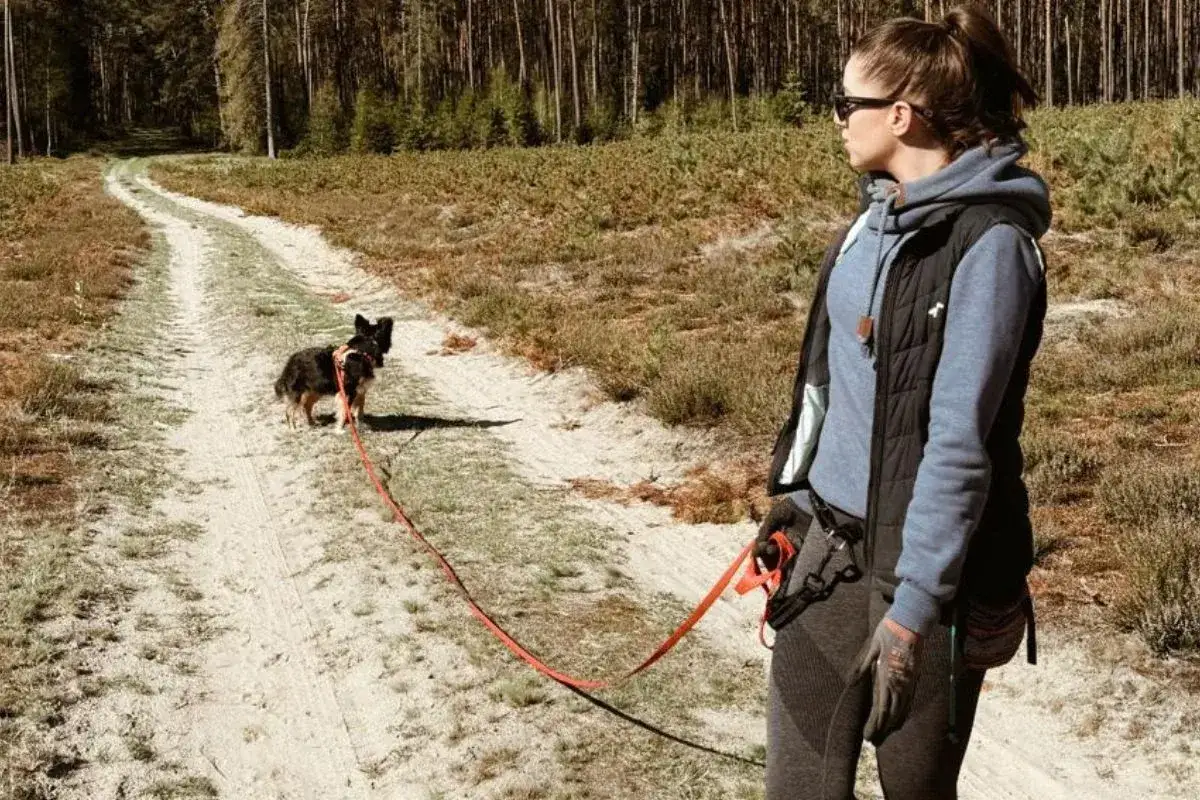 Kobieta z psem na smyczy na leśnej ścieżce. Wygodny strój i saszetka to podstawa, gdy zastanawiasz się, co wziąć na spacer z psem.