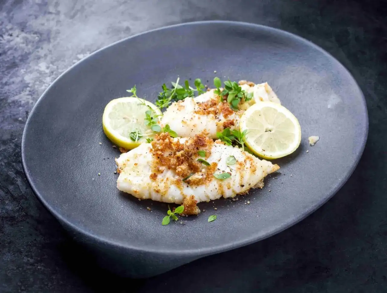Calamares a la plancha con lim&oacute;n, cubiertos con pan rallado crujiente y hierbas frescas, servidos en un plato oscuro.