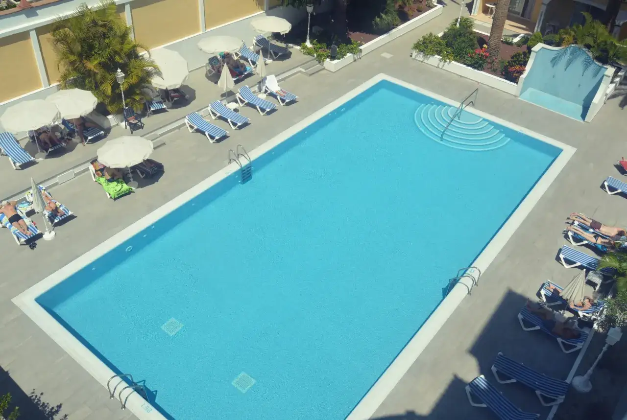 Piscina azul brillante en el hotel San Borondon, con tumbonas y sombrillas. Gente relajándose al sol.