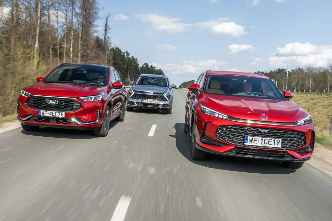 Trzy SUV-y jadące drogą: czerwony Ford, szary Kia Sportage Hybrid i kolejny czerwony SUV.