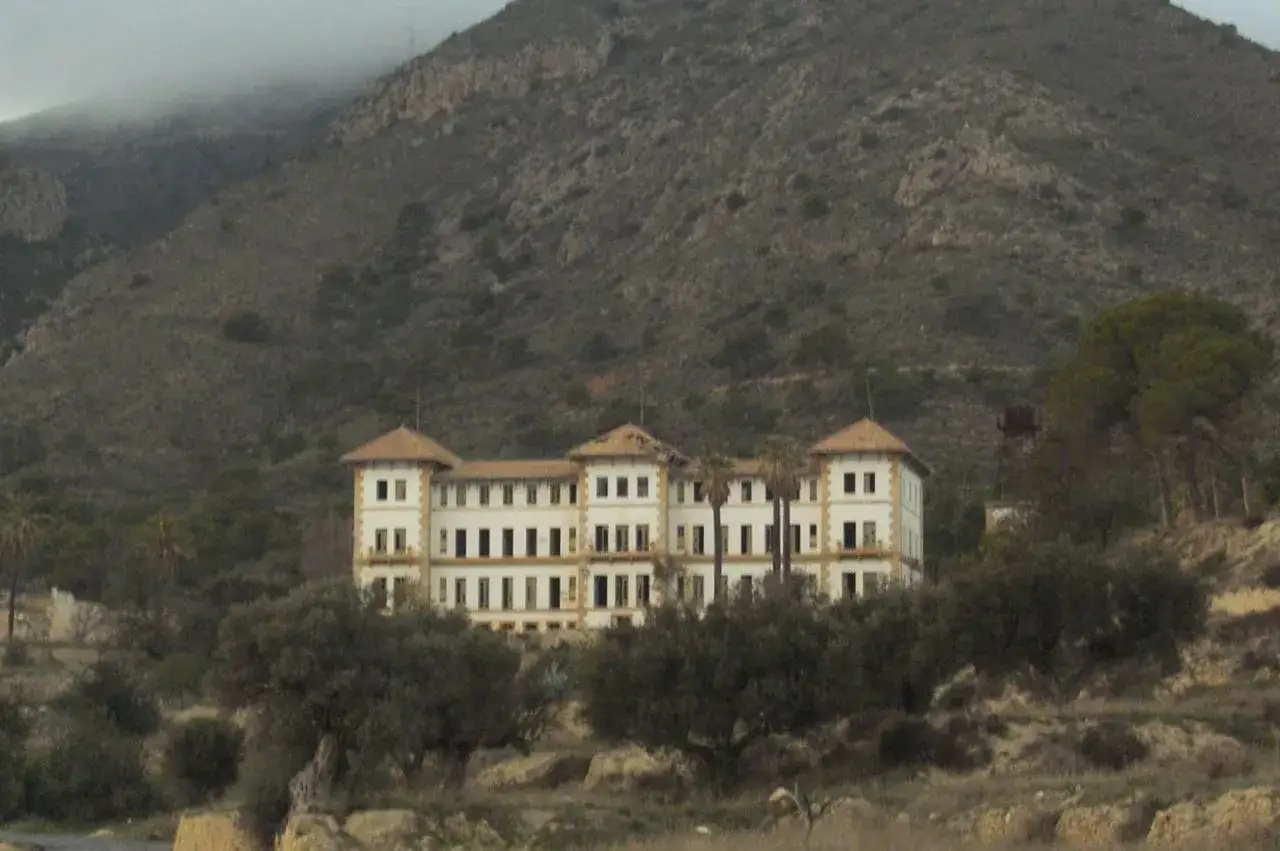 El imponente edificio del preventorio Aguas de Busot se alza contra una ladera montañosa, evocando historias del pasado.