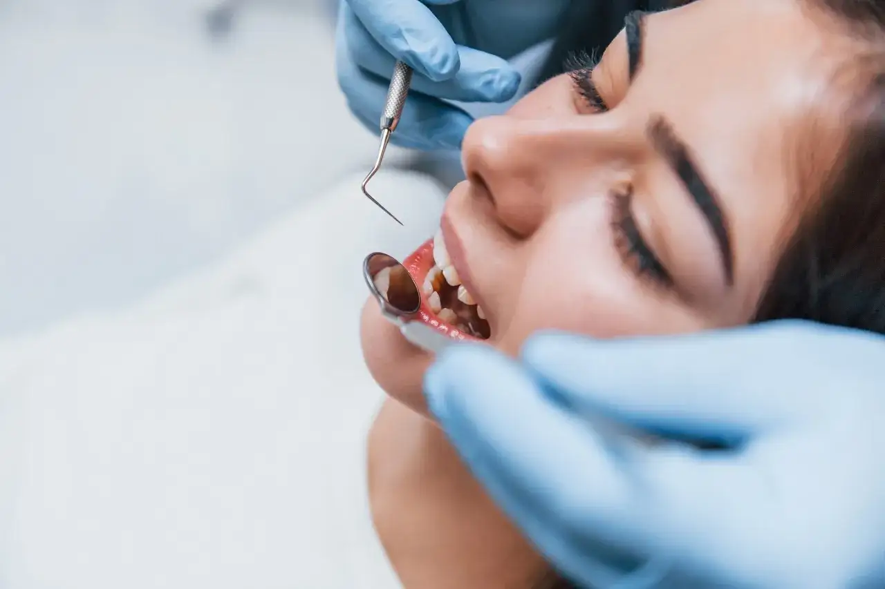 Dentysta bada zęby pacjentki, sprawdzając czy nie ma ubytków klinowych.