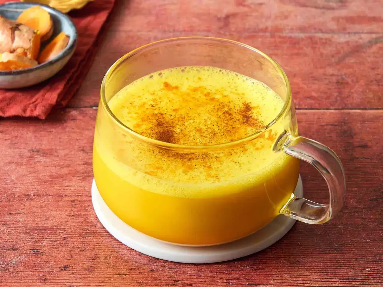 Goldene Milch in einer Tasse, ein Getr&auml;nk, das zeigt, wozu Kurkuma gut ist. Daneben frische Kurkumawurzeln.